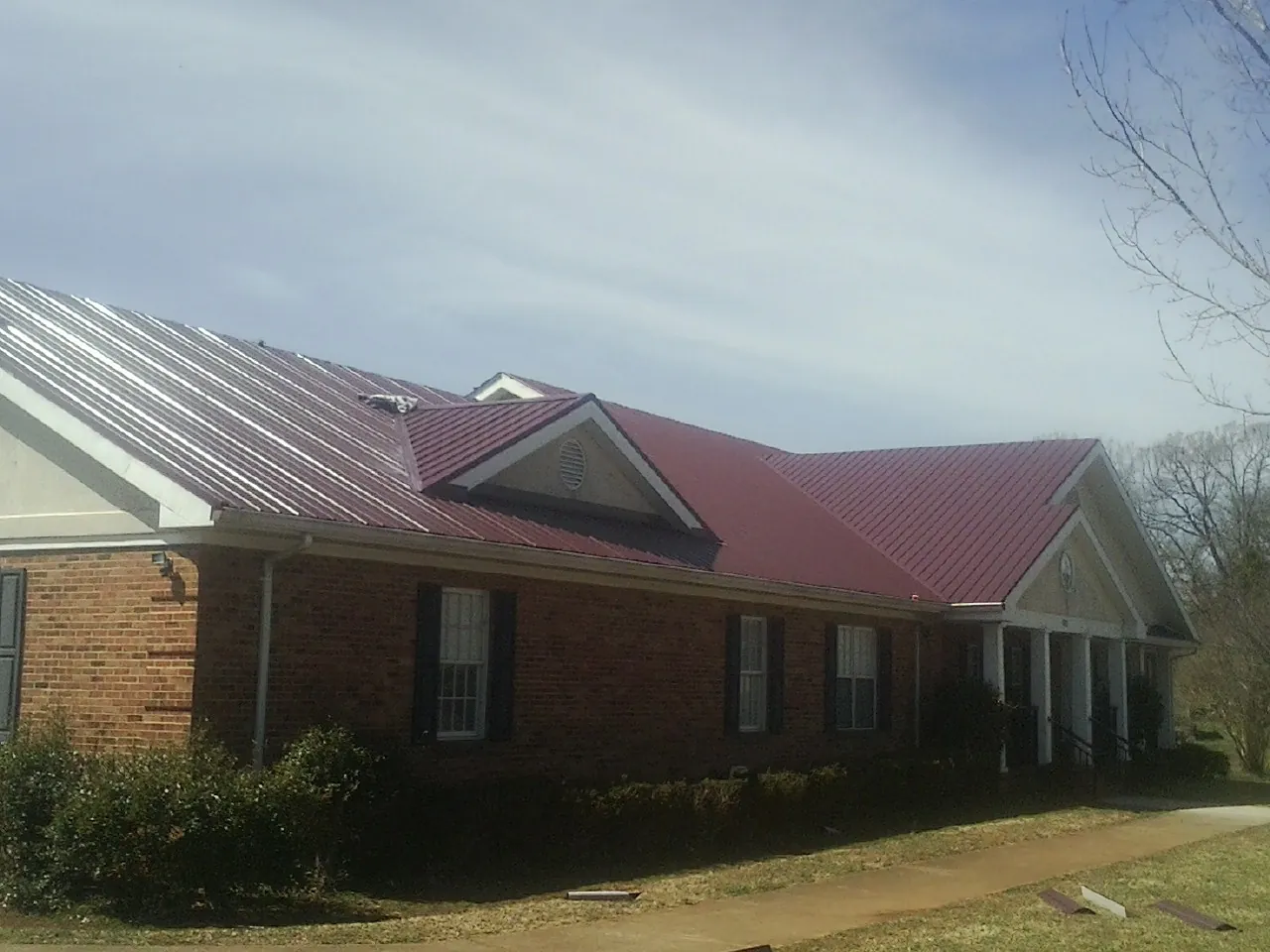 Red metal roof with gabled entries on a long brick building, from a Hail Damage Roof Repair job in Belford
