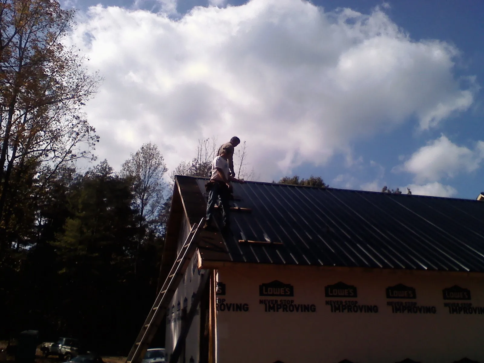 Roofer fastening dark metal panels high against a cloudy sky, from a Roof Inspection job in Belford
