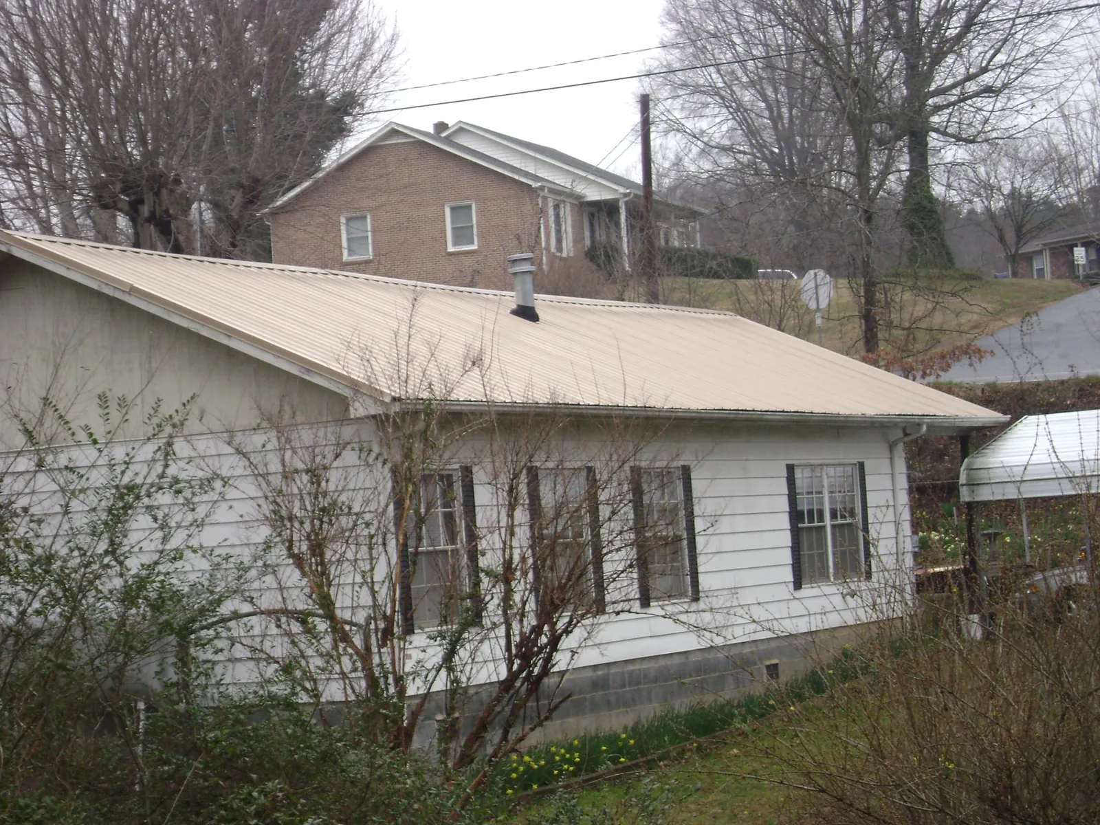 Tan metal roof on a white sided house set into a hillside — Commercial Roofing by Roofing Brothers in Belford