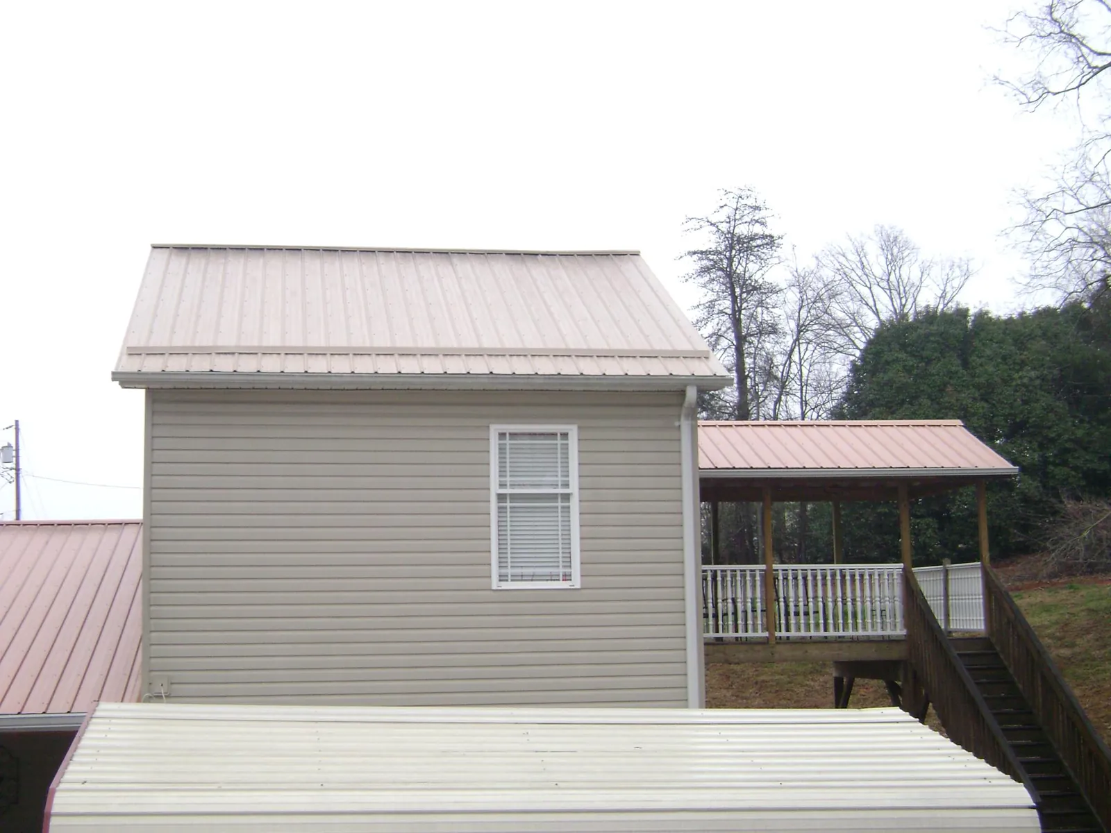 Tan metal roofs on a two story addition and attached porch, from a Roof Replacement job in Belford